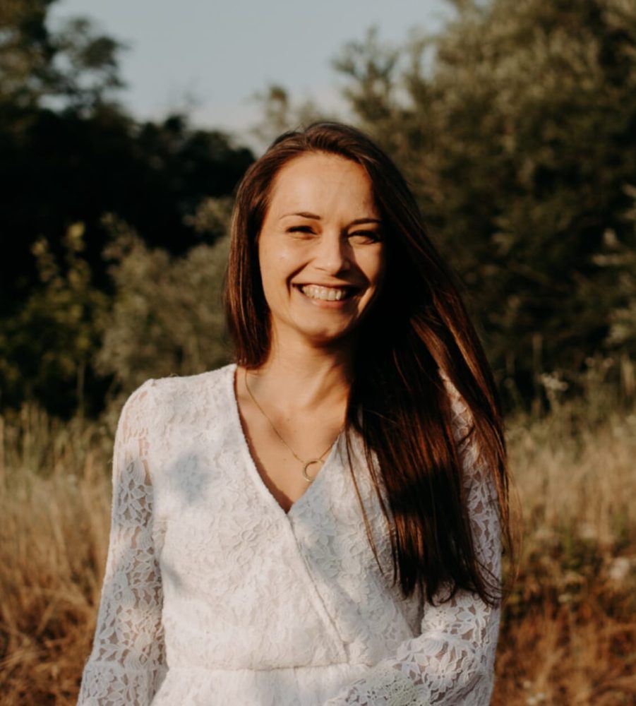 Anne-Claire Brosset, souriante, en robe blanche dans un champ au soleil couchant
