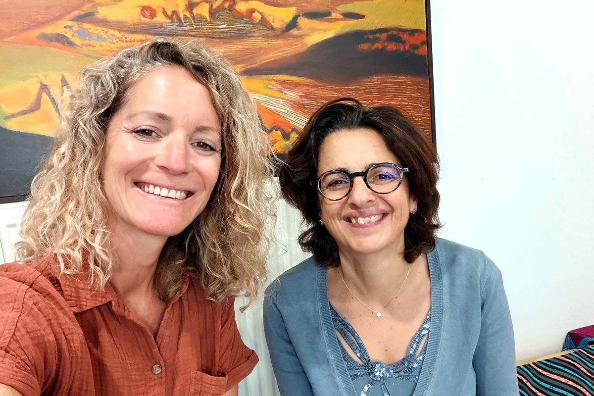 Laure Hambenne et Corinne Haddad, souriantes, assises côte à côte devant un tableau aux couleurs chaudes